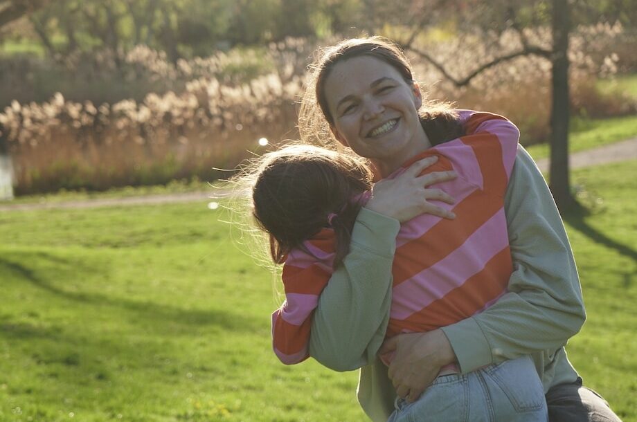 Laura Horvath, die Gründerin von fini, lacht herzlich und umarmt ihre Tochter Fini im Freien auf einer Wiese im Donaupark in Wien.